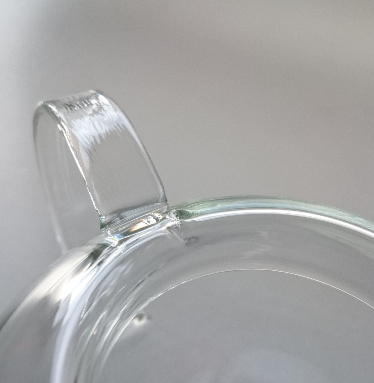 Close-up view of the Manmaru glass teapot handle, showcasing the smooth and seamless craftsmanship of the transparent borosilicate glass.