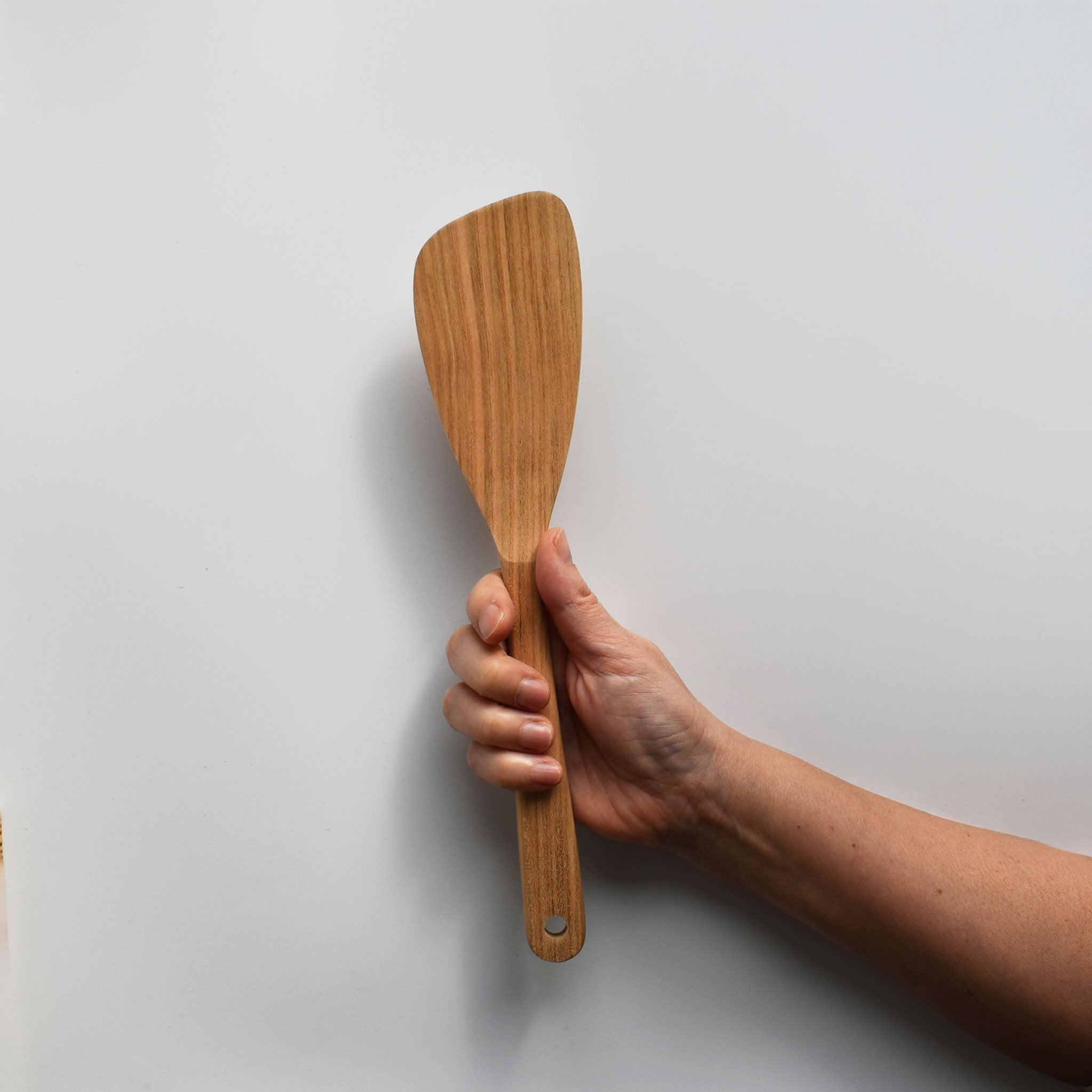 Sakura wood angled spatula with natural wood grain held by hand against a white background