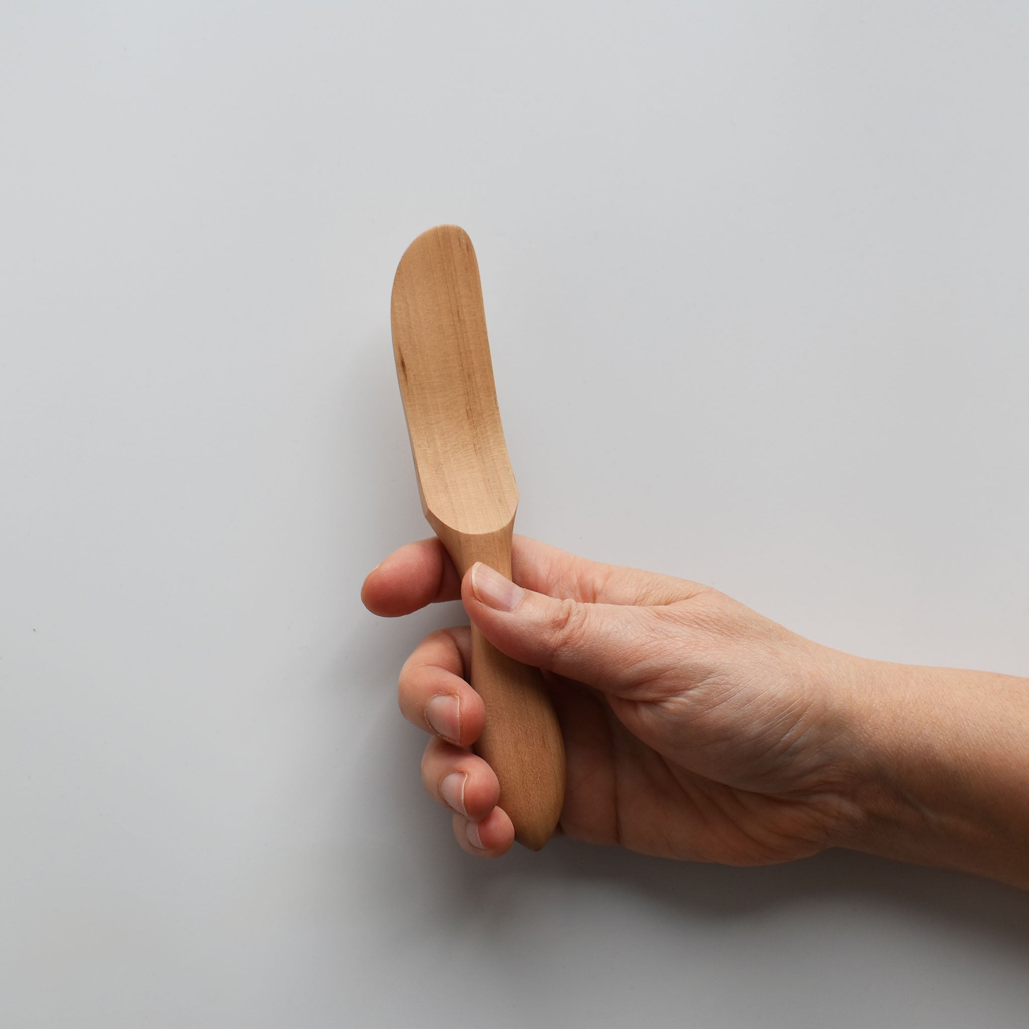 Sakura wood butter knife with smooth carved handle and natural wood grain held by hand for scale