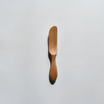 Sakura wood butter knife with smooth carved handle and natural wood grain on a white background