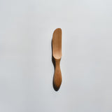 Sakura wood butter knife with smooth carved handle and natural wood grain on a white background