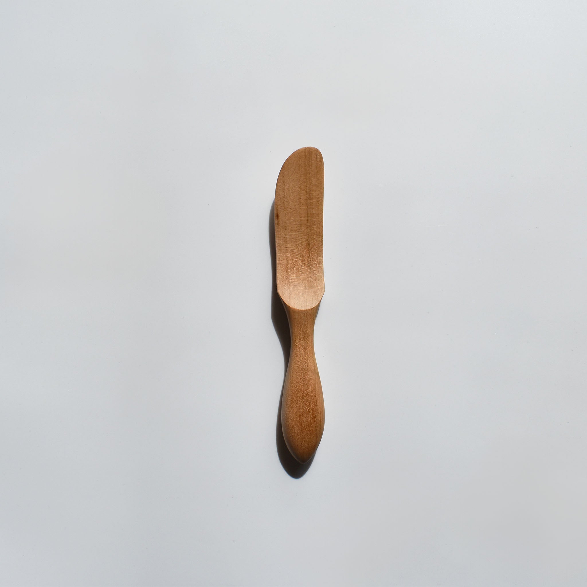 Sakura wood butter knife with smooth carved handle and natural wood grain on a white background