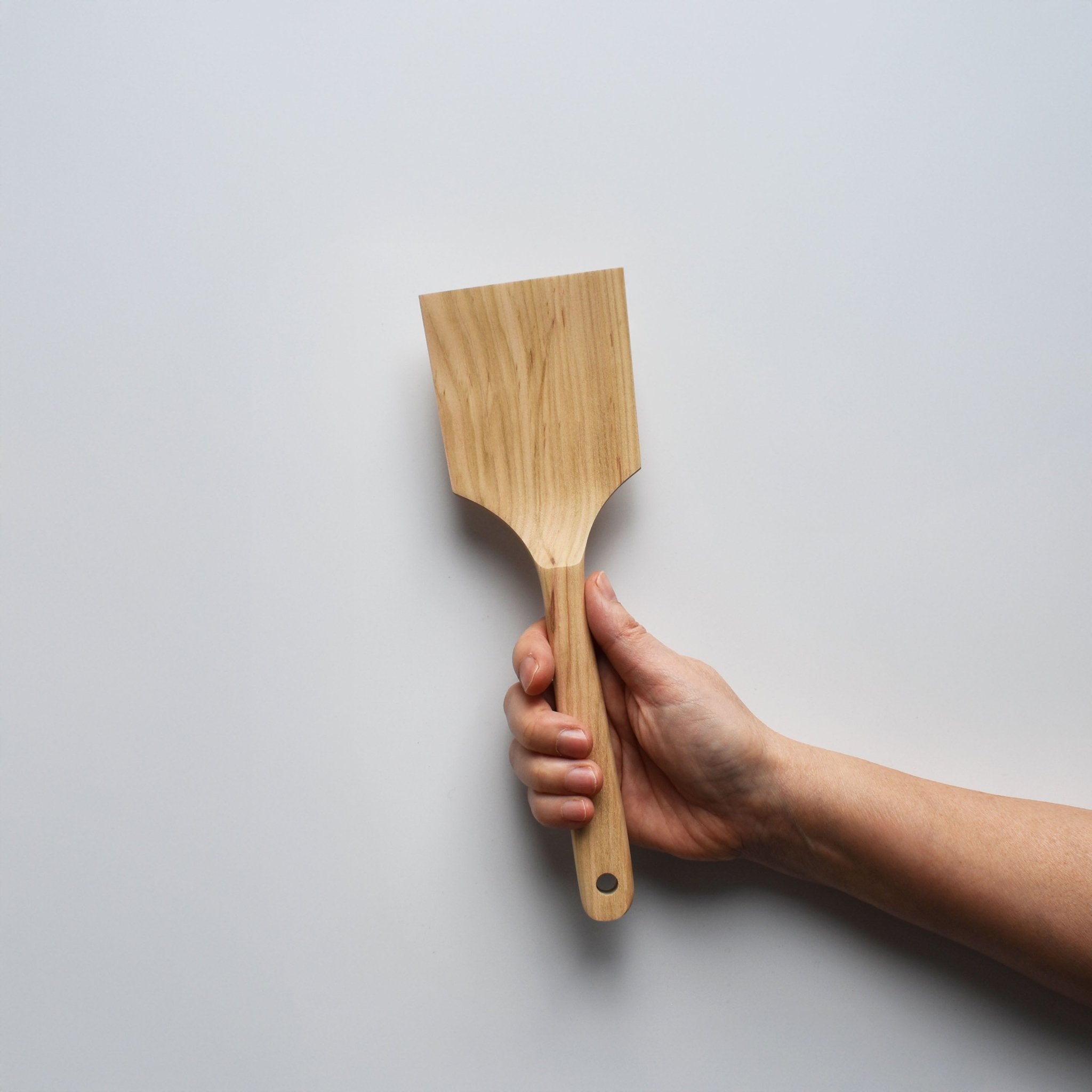Sakura wood flat spatula with wide paddle shape and natural wood grain held by hand for scale