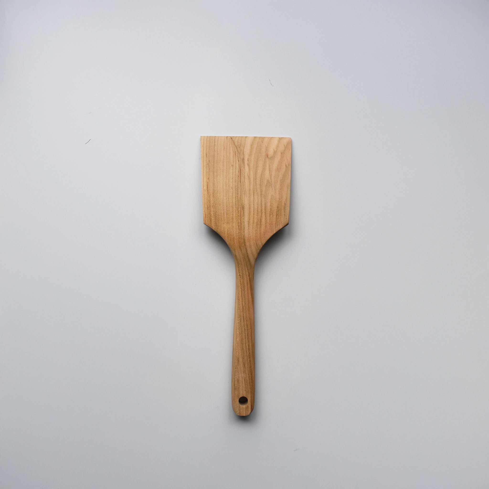 Sakura wood flat spatula with wide paddle shape, hanging hole, and natural wood grain on a white background