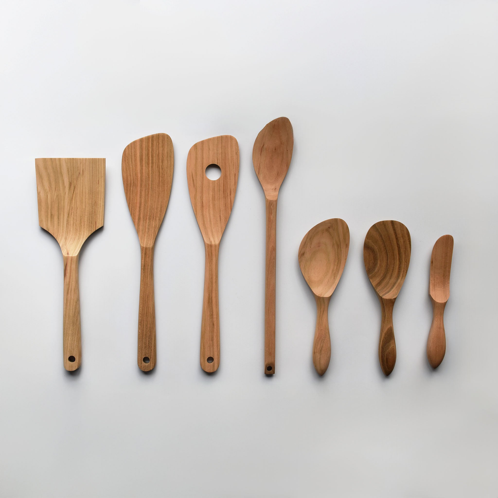 Sakura wood Japanese kitchen utensil set with spatulas, spoons, and cooking tools arranged on a white background