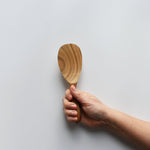 Sakura wood round rice paddle with smooth carved bowl and natural wood grain held by hand for scale