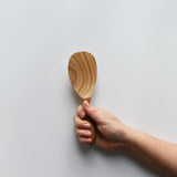 Sakura wood round rice paddle with smooth carved bowl and natural wood grain held by hand for scale