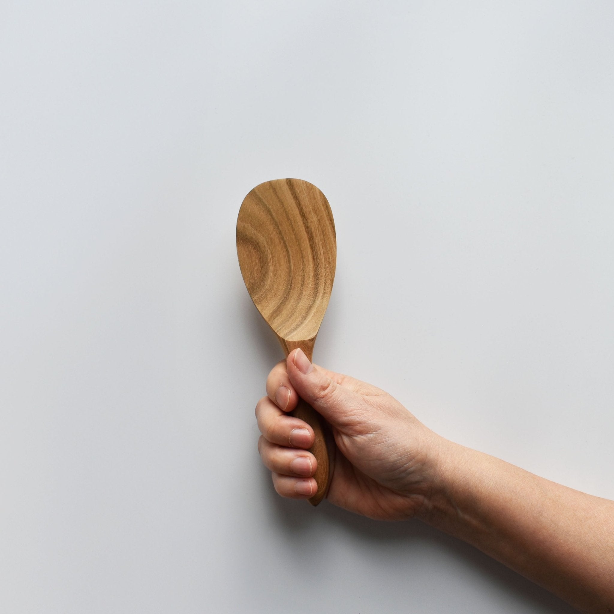Sakura wood round rice paddle with smooth carved bowl and natural wood grain held by hand for scale