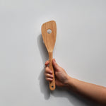 Sakura wood slotted spatula with hanging hole and natural wood grain held by hand for scale