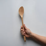 Sakura wood soup spatula with long handle and smooth carved spoon shape held by hand for scale
