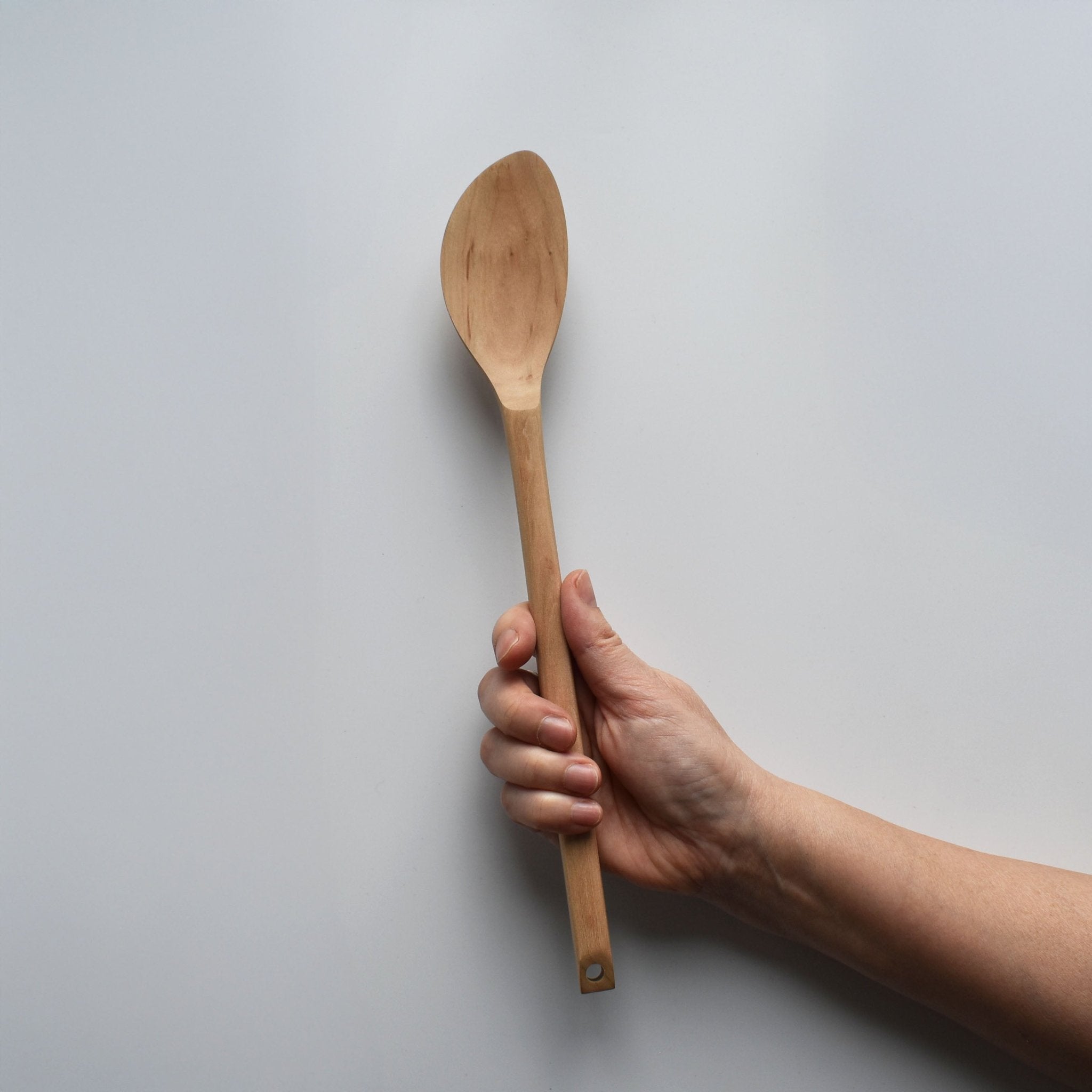 Sakura wood soup spatula with long handle and smooth carved spoon shape held by hand for scale