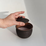 Shigaraki artisan black salt pot with textured ceramic finish, salt inside, and removable lid held open by hand