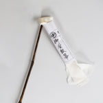 Traditional Japanese silk duster with a bamboo handle and white silk strips, shown with its paper wrapping featuring Japanese calligraphy.