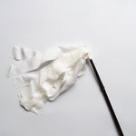 Japanese silk duster with flowing white silk strips and a dark bamboo handle, laid on a white background.