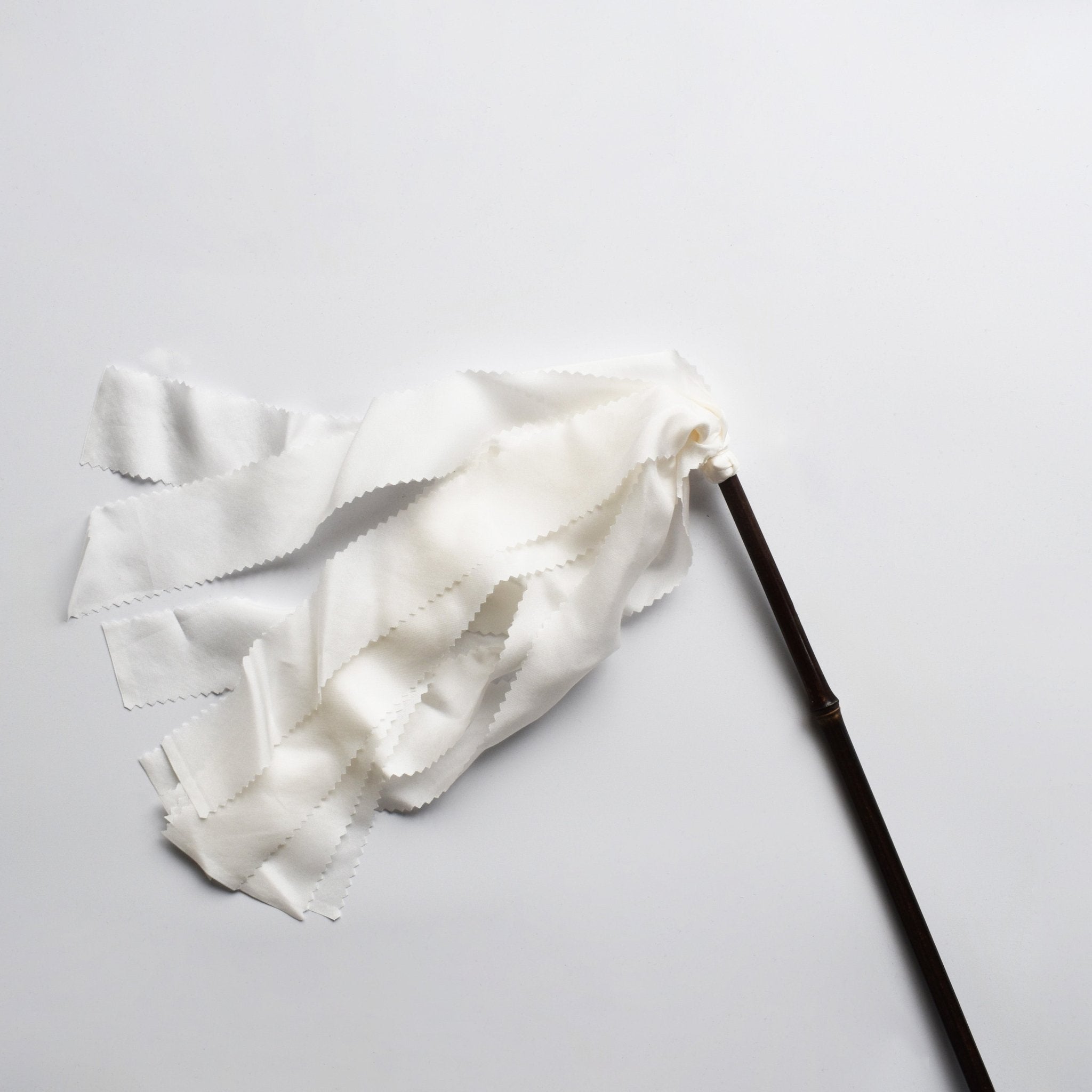 Japanese silk duster with flowing white silk strips and a dark bamboo handle, laid on a white background.