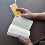 Toast Bookmark. A person holding a book and using a hyper-realistic toast-shaped bookmark made by Nagao Shokken, a Japanese artisan known for food sample-inspired accessories.”