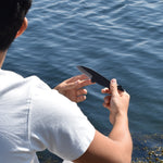 A person holding the Tosa Bryde’s Whale Knife near the ocean, examining its blade under natural sunlight.
