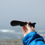 A person holding a black Tosa Sperm Whale Knife against a misty coastal backdrop