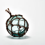 Vintage Japanese glass fishing float wrapped in traditional hand-tied rope netting, featuring a seafoam green hue and natural imperfections that add rustic coastal charm