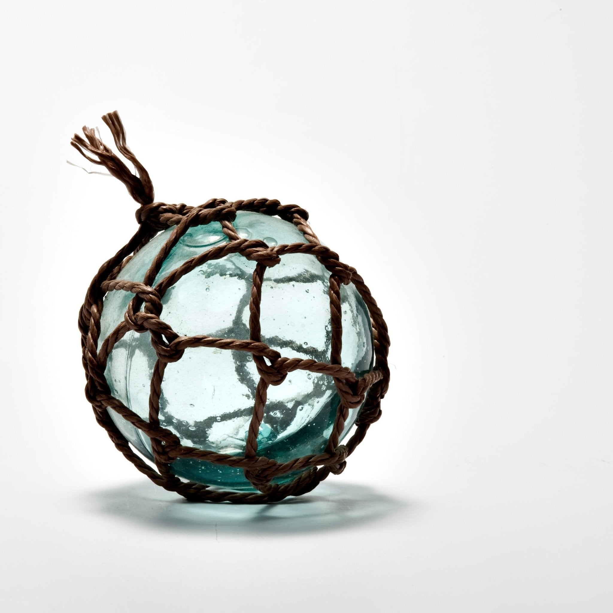 Vintage Japanese glass fishing float wrapped in traditional hand-tied rope netting, featuring a seafoam green hue and natural imperfections that add rustic coastal charm