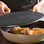 Person lifting a splatter screen off a frying pan with sizzling chicken thighs, showing how it controls oil splatter while cooking meat on the stovetop