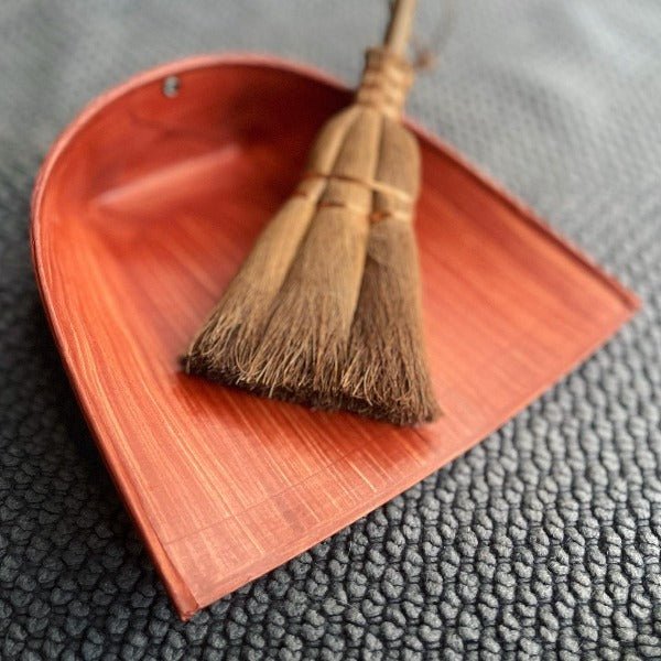 Close-up of a traditional Japanese Harimi dustpan made from persimmon-coated washi paper, paired with a natural Shuro palm broom resting on textured fabric