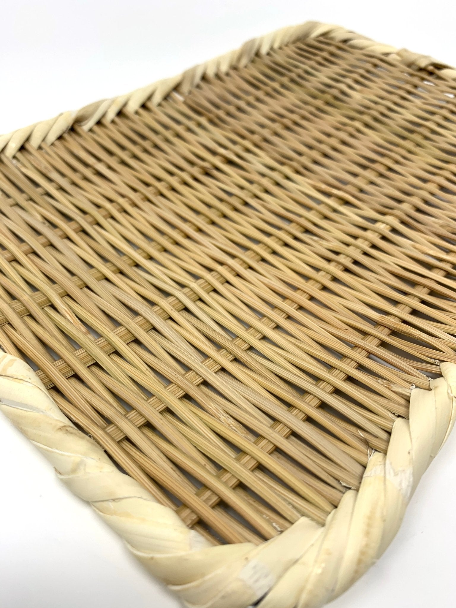 Angled close-up of a handwoven rectangular bamboo zaru colander with a twisted rim, showcasing the fine basket weave and natural fiber texture on a white background