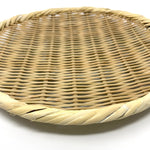 Angled close-up of a round bamboo zaru colander showing detailed weave and rim pattern on a white surface