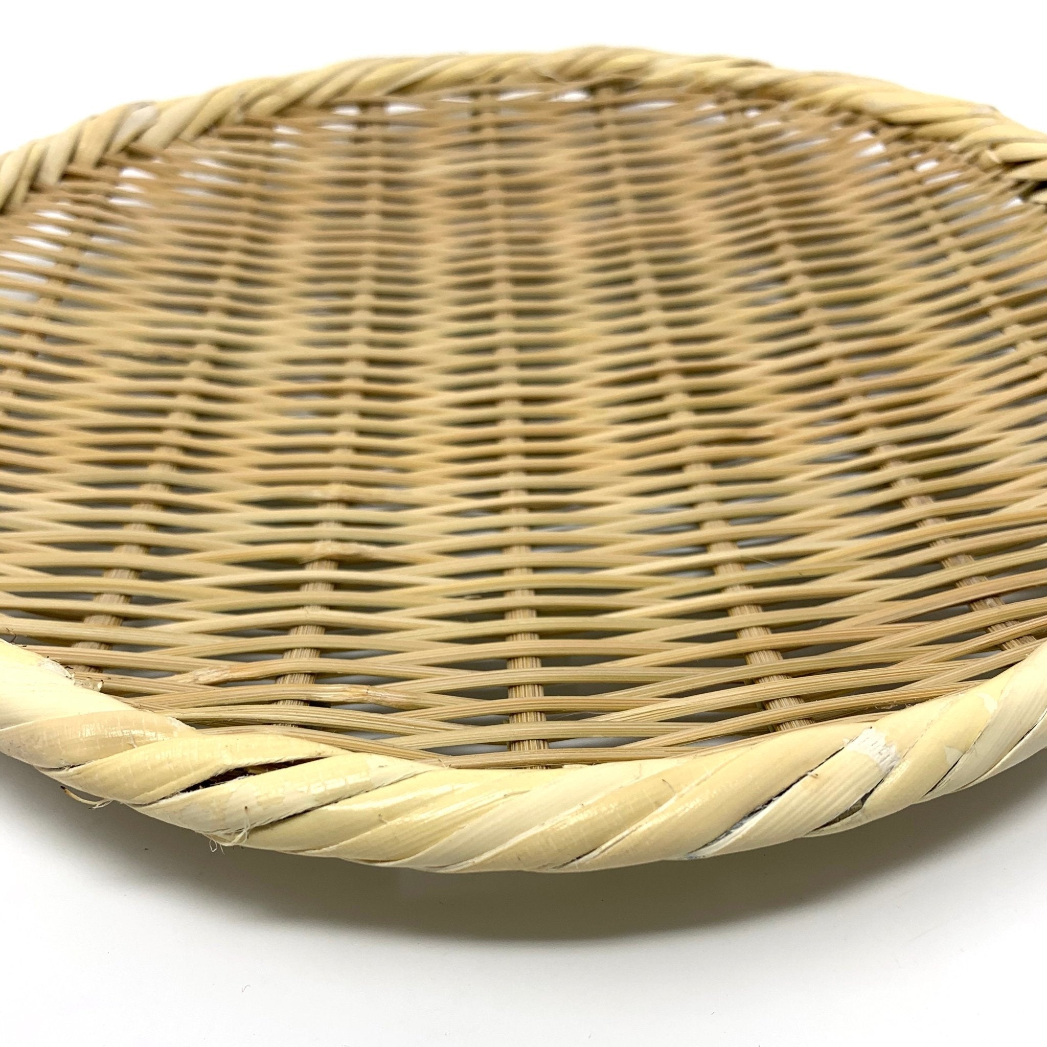 Angled close-up of a round bamboo zaru colander showing detailed weave and rim pattern on a white surface