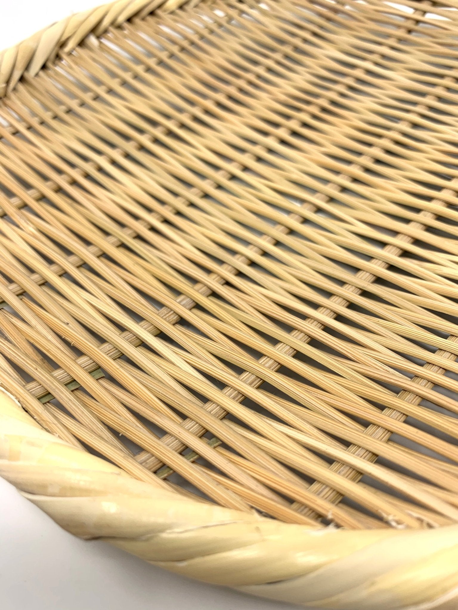 Extreme close-up of the woven bamboo surface and twisted rim of a round Japanese zaru colander on a white background