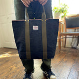 Person holding a Japanese selvage denim tote by Thread Line in a sunlit room, showing olive green handles and casual everyday style