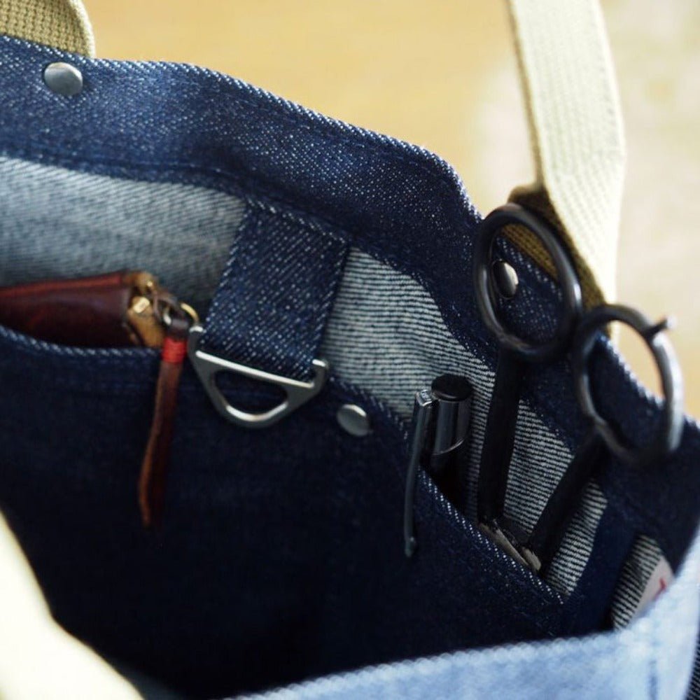 Close-up of interior denim tote showing organized compartments with scissors, pens, wallet, and D-ring loop for key or tool attachment