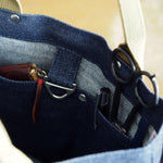 Close-up of interior denim tote showing organized compartments with scissors, pens, wallet, and D-ring loop for key or tool attachment
