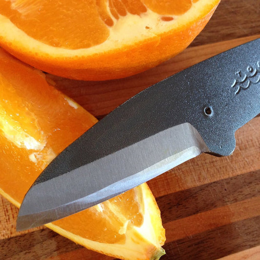 Close-up of the Bryde’s Whale Kujira knife slicing an orange on a wooden cutting board, highlighting the sharp carbon steel blade and fine craftsmanship
