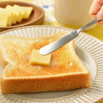 A slice of butter from the Japanese slicer being spread onto toasted bread with a butter knife—perfectly portioned for a cozy breakfast moment.