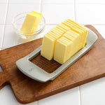 Butter block cleanly sliced into uniform pieces using a Japanese butter slicer, displayed on a cutting board with portioned slices in a glass bowl.