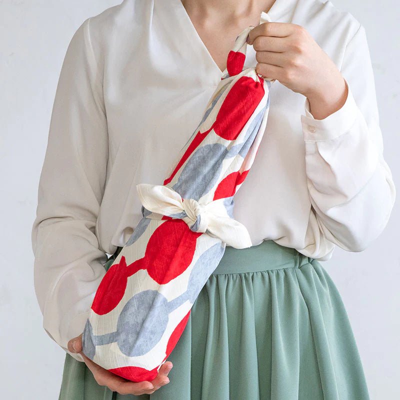 Woman holding a wine bottle wrapped in colorful Yumeji Takehisa Tsunagi Dango furoshiki cloth, showcasing traditional Japanese gift wrapping.