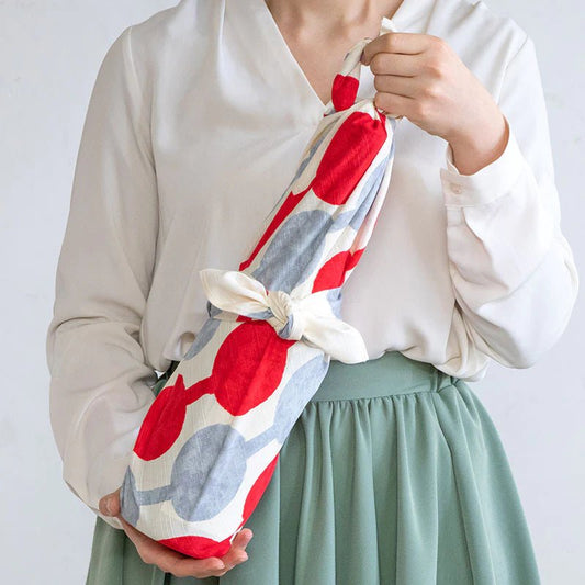 Woman holding a wine bottle wrapped in colorful Yumeji Takehisa Tsunagi Dango furoshiki cloth, showcasing traditional Japanese gift wrapping.