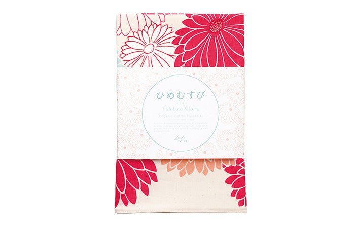 A folded furoshiki cloth from the Hime Musubi series designed by Adeline Klam, featuring a bold pink and red garbera flower pattern. The cloth is neatly packaged with a label written in Japanese and English, showcasing it as an organic cotton furoshiki. The visible floral design includes layered petals in vivid pink, red, and coral on a soft off-white background.