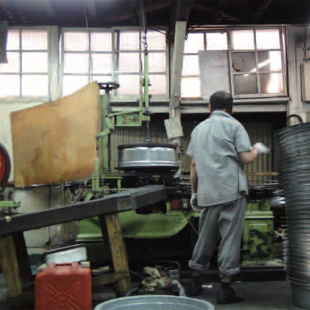 Japanese metalworker operating machinery inside a traditional factory workshop, producing aluminum products with industrial tools and precision