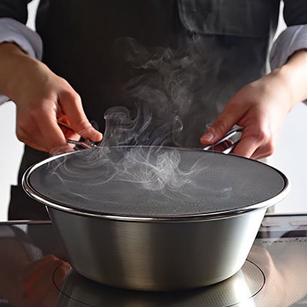 Person using a Japanese stainless steel splatter screen over a steaming pot on the stove, demonstrating how it prevents oil and liquid splashes during cooking