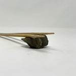 Minimalist display of traditional Japanese bamboo chopsticks resting on a natural stone chopstick rest, photographed on a white surface to highlight texture and balance in design