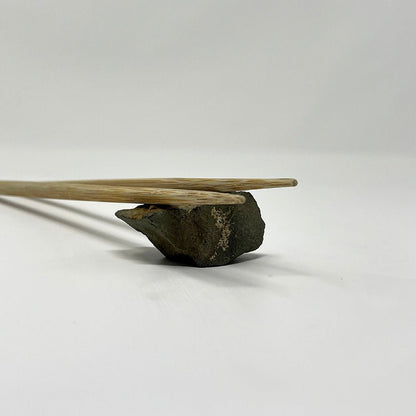 Minimalist display of traditional Japanese bamboo chopsticks resting on a natural stone chopstick rest, photographed on a white surface to highlight texture and balance in design