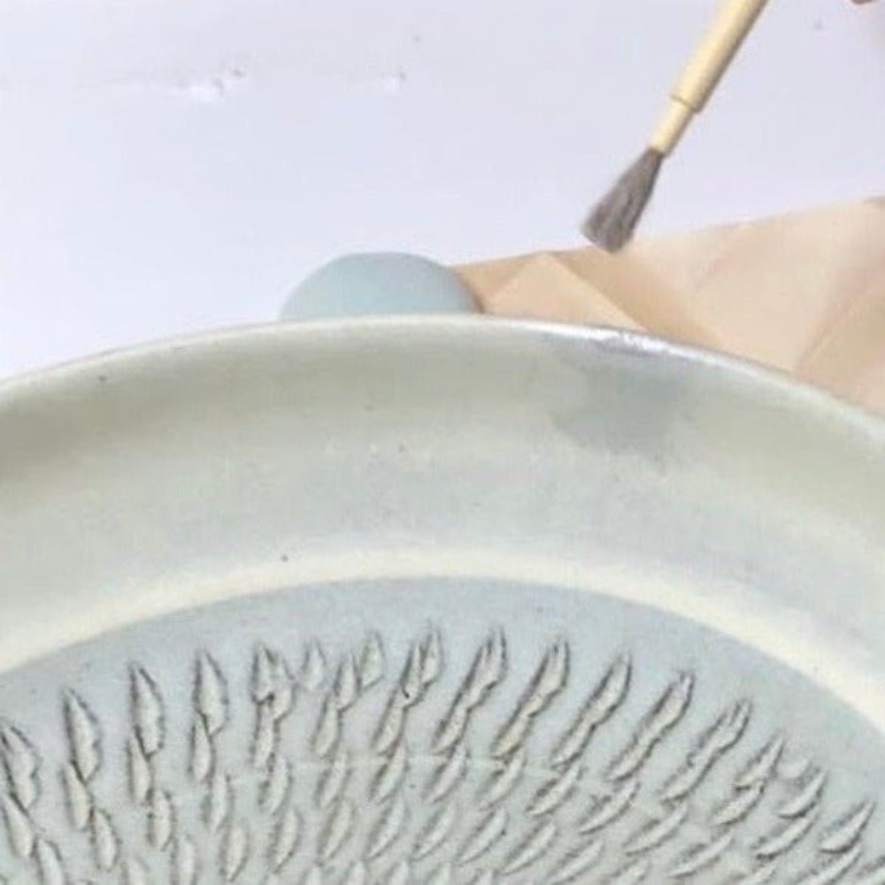 Applying urushi lacquer to a chipped ceramic plate with a traditional brush—Kintsugi repair process in progress.