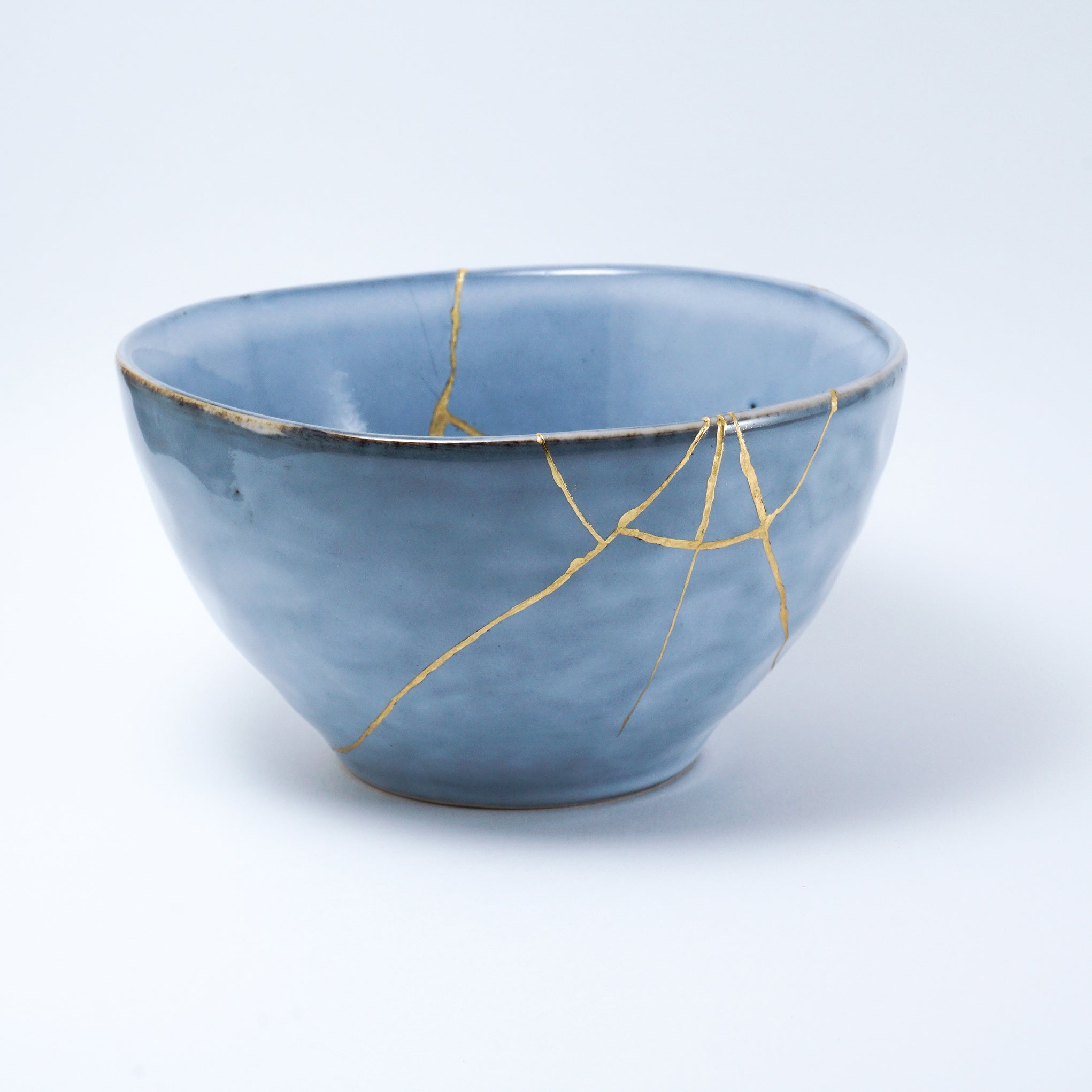 Blue ceramic bowl repaired with gold using the traditional Japanese Kintsugi technique, showcasing beauty in imperfection.