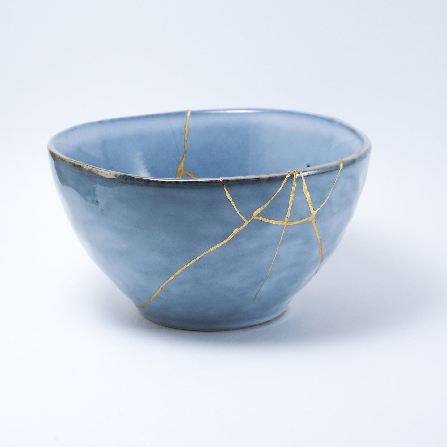 Blue ceramic bowl repaired with gold using the traditional Japanese Kintsugi technique, showcasing beauty in imperfection.