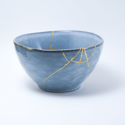 Blue ceramic bowl repaired with gold using the traditional Japanese Kintsugi technique, showcasing beauty in imperfection.