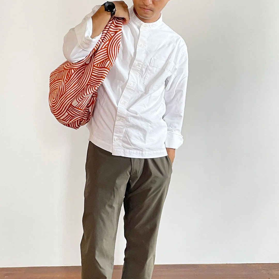 Man wearing a white button-up shirt and olive trousers, carrying a bold persimmon orange and white furoshiki bag with modern wave patterns over his shoulder. 