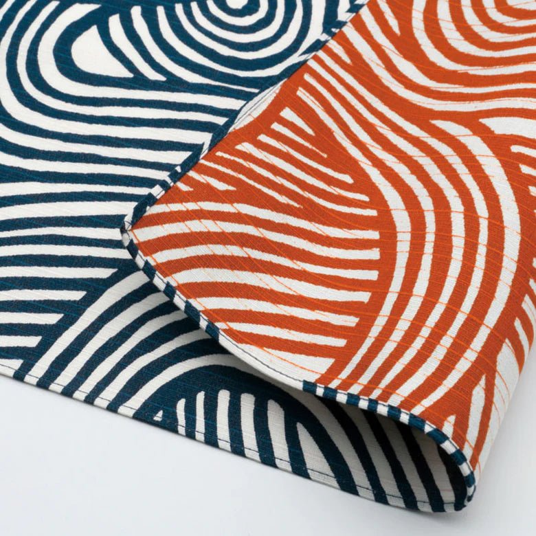 Close-up of reversible Japanese furoshiki cloth featuring bold wavy line patterns in indigo blue and persimmon orange on white cotton fabric.