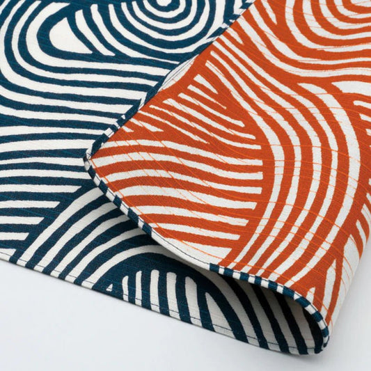 Close-up of reversible Japanese furoshiki cloth featuring bold wavy line patterns in indigo blue and persimmon orange on white cotton fabric.